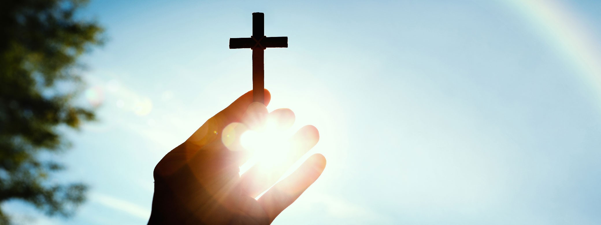 Hand mit Kreuz in der Hand vor dem Himmel