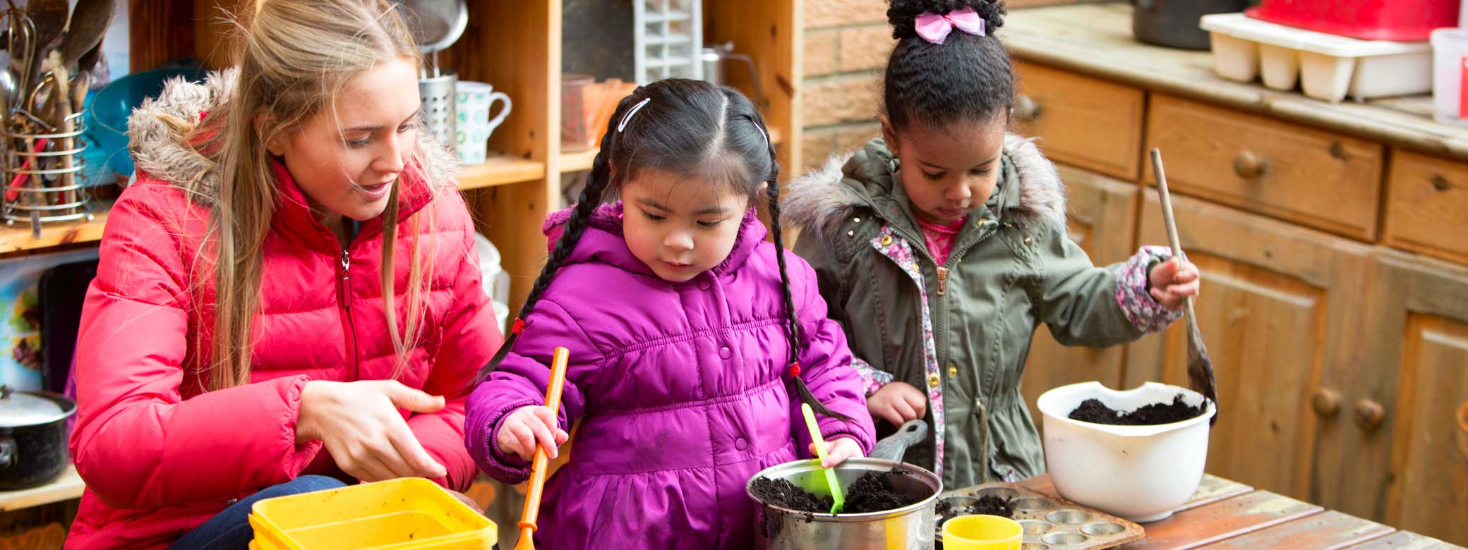 Kinder spielen mit Erzieherin in Matschküche
