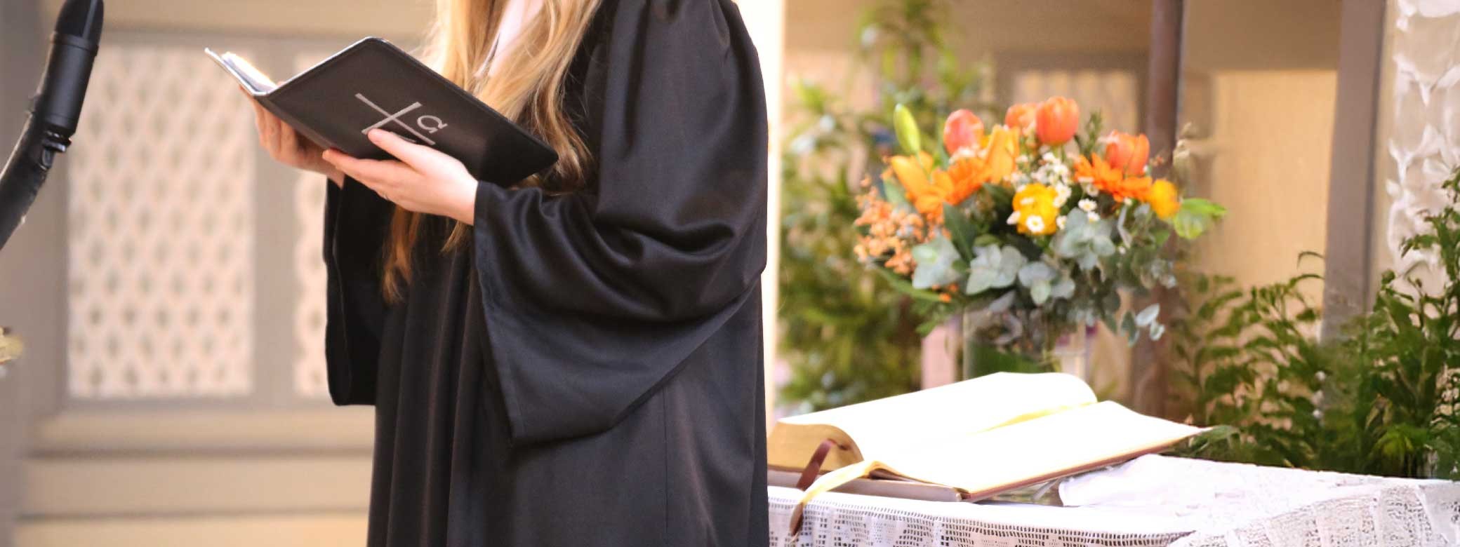 Pastorin, die aus der Bibel vorliest mit Kirchraum im Hintergrund